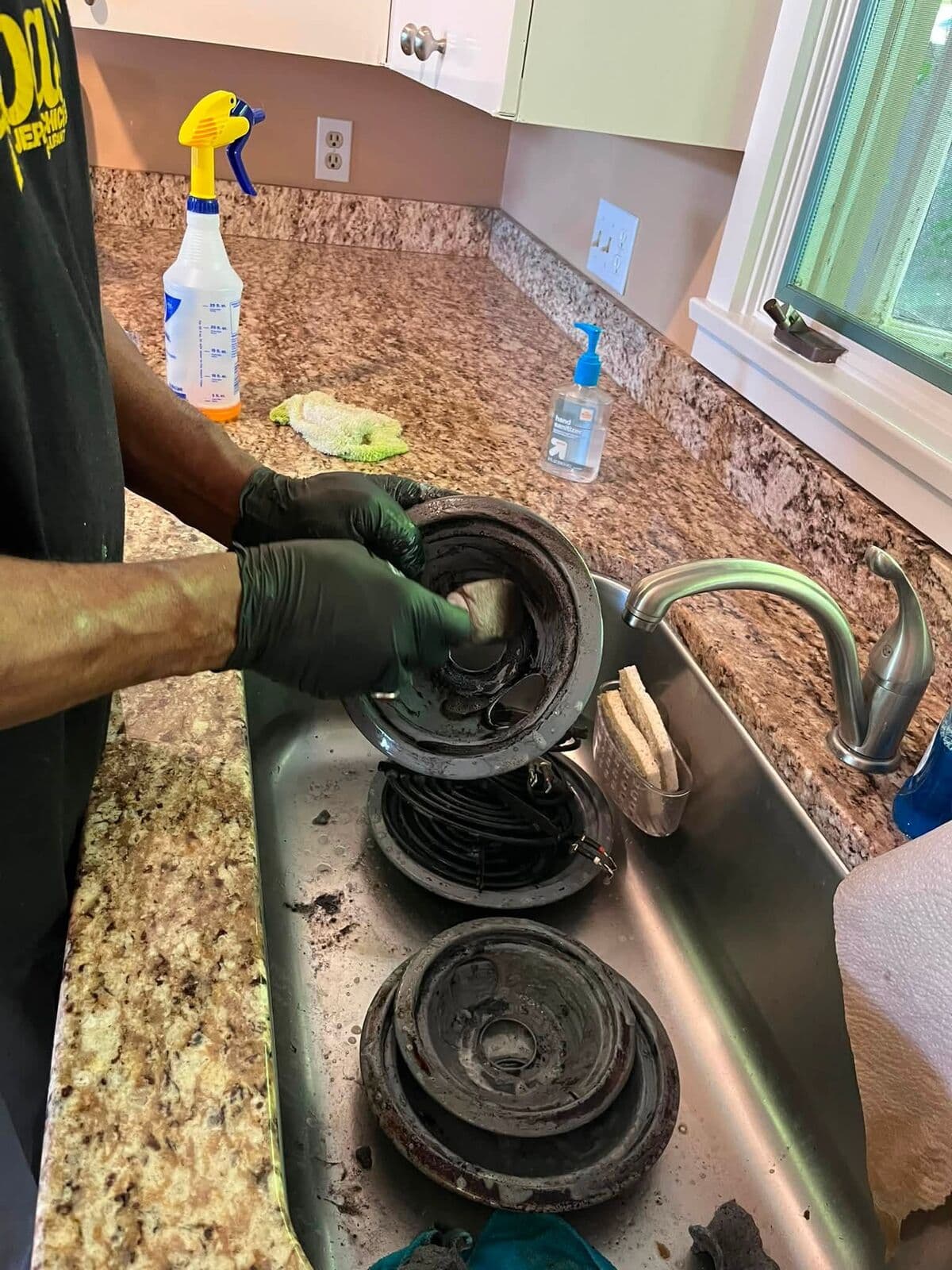 Gloved hands scrubbing stovetop parts
