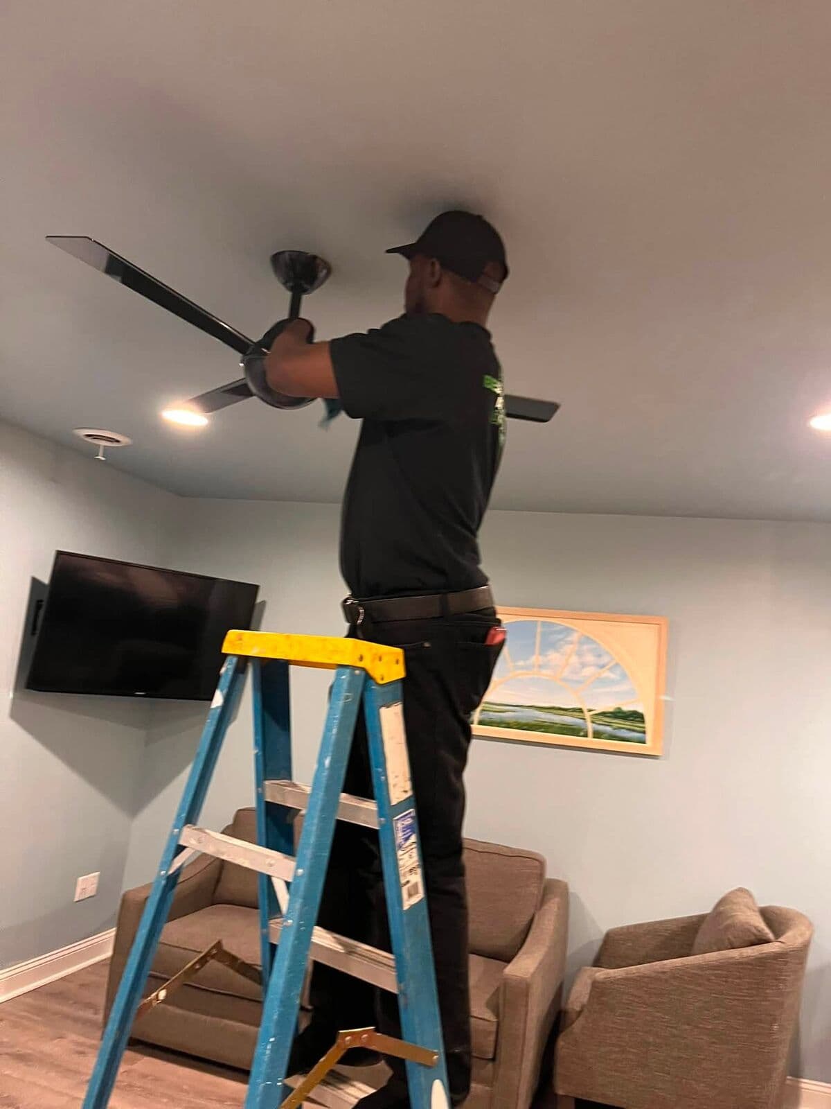 Crew member on a ladder cleaning a ceiling fan